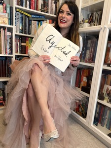 An image of a woman in a chair wearing a pink tulle skirt holding a notebook open with handwritten words 'Agented Future Author'