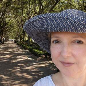 Sara Amis standing in front of an avenue lined with trees, wearing a blue hat