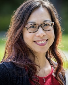 Photo of Mai-Linh Hong, a Southeast Asian American woman with long wavy hair and glasses. 