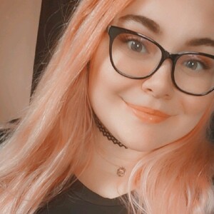 alt="Smiling girl with rose gold hair and glasses, indoors with soft lighting"