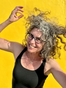 Andrea in a black tank top fluffing up her hair with a yellow background.