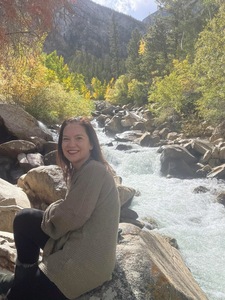 An author sitting peacefully in nature next to a flowing brook.
