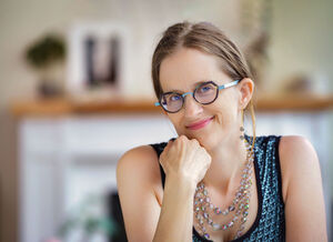 Woman with hair pulled back, wearing glasses and a small smile
