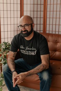 Photo of the author in a studio wearing a black band t-shirt and thick glasses.