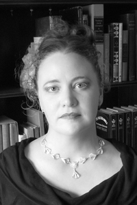 Black and white photo of Bryn Greenwood, a white woman with frizzy hair, seated in front of several shelves full of books.