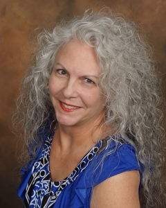 Photo of author Fiola Faelan sporting long, curly silver locks and wearing a shiny royal blue cap-sleeve dress