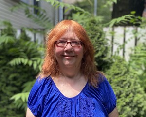 I am standing in a garden. I'm wearing a blue top, and I'm white (Irish American) with red hair and blue eyes. 