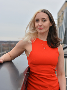 Woman standing on balcony in red shirt, with half brown and half blonde hair (no text)
