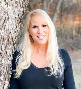 Blonde hair author in a black shirt standing against a tree